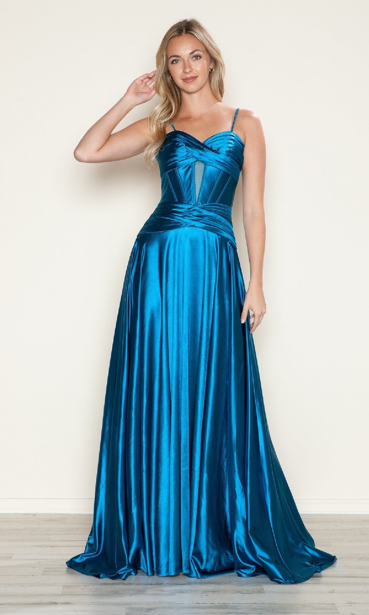 A woman poses on a wooden floor against a light wall, wearing the Cut-Out Long A-Line Prom Dress: Poly USA 9700, featuring shiny teal blue satin fabric with spaghetti straps and a fitted bodice.